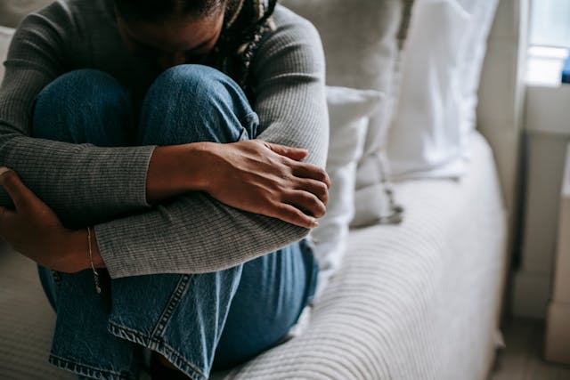 woman on bed arms wrapped around knees